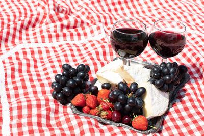 Summer picnic on a green lawn with red wine, cheese and fresh berries, grapes