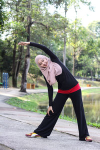 Portrait of mid adult woman wearing hijab while exercising by lake at park