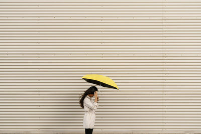 Woman holding umbrella by white corrugated wall