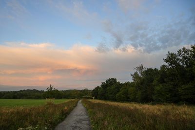 Empty road amidst field against sky