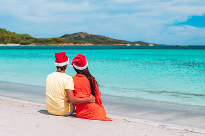 Rear view of couple sitting on beach by sea against sky