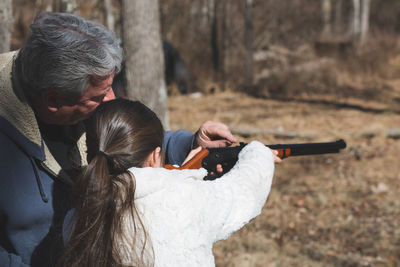 Man assisting girl using gun while standing on field