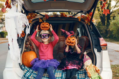 Cute girls wearing costume sitting in car trunk