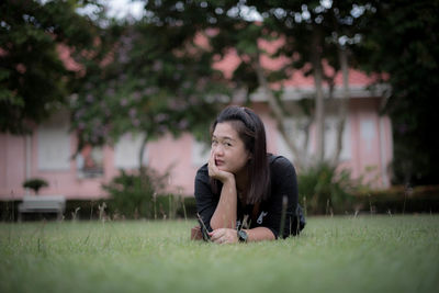 Portrait of young woman sitting on grass against trees