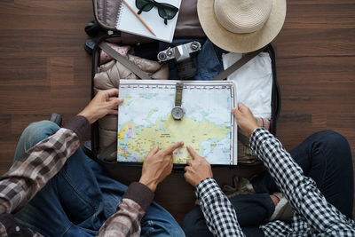 High angle view of man and woman pointing on map over packed suitcase while sitting on floor