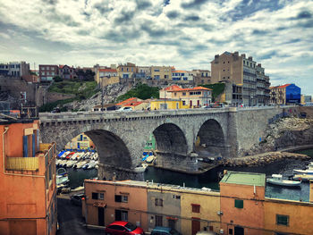 Bridge over river by buildings in city against sky