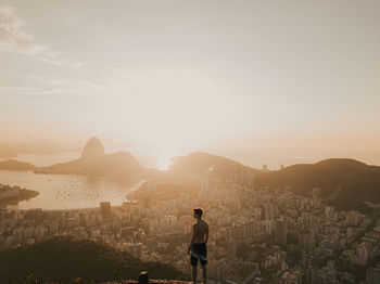 Woman standing on sidewalk by cityscape against sky during sunset