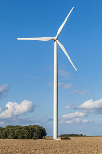 Wind turbine on field against blue sky