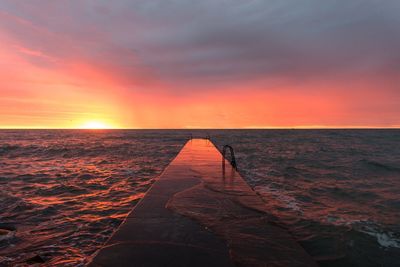 Pier amidst sea against cloudy orange sky during sunset