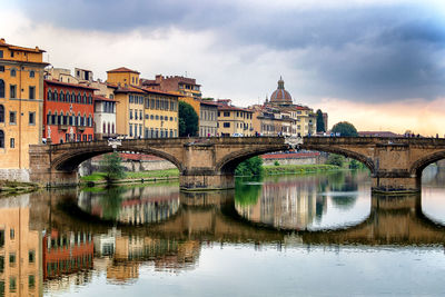 Arch bridge over river by buildings against sky in city