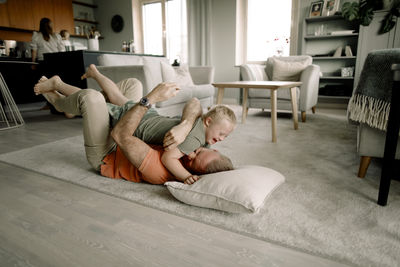 Full length of father lying on carpet while embracing son in living room at home