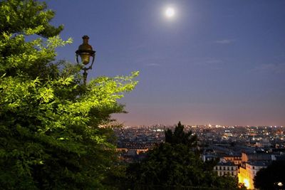 Illuminated street light and buildings in city against sky at dusk
