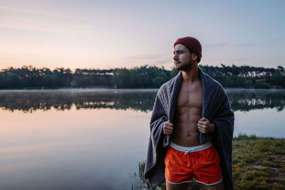 Serious guy at the forest near the water and preparing for the swimming in the cold lake at morning