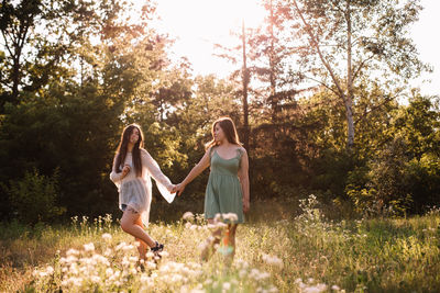 Lesbian couple holding hands while walking in forest in summer