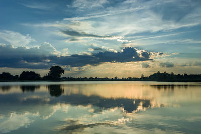 Sun behind a cloud over a lake, trees on the horizon, evening view