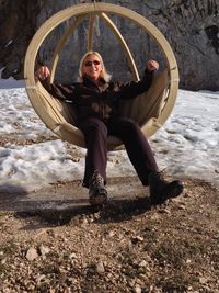 Mature woman sitting on swing at snow covered mountain