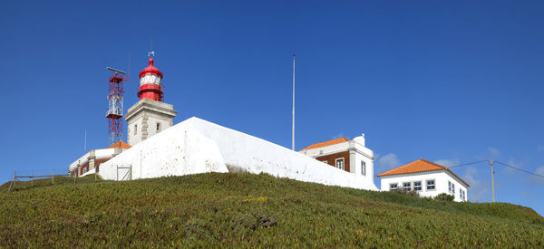 Low angle view of lighthouse amidst buildings against clear blue sky