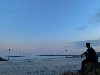 Man looking at suspension bridge over sea against sky