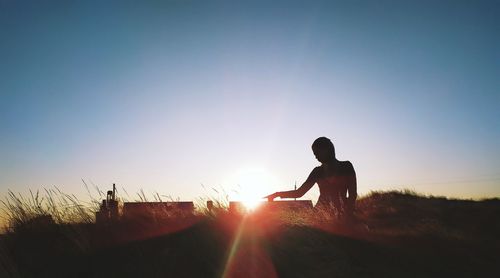 Silhouette woman sitting on field against sky during sunset