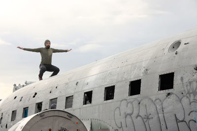 Low angle view of man with arms outstretched standing against sky