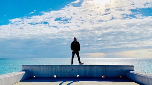 Full length of man standing against seascape and cloudy sky