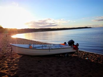 Motorboat on shore at beach against sky during sunset