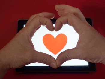 Cropped hands making heart shape over device screen