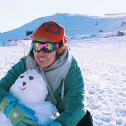Smiling woman wearing warm clothing embracing snowman during winter
