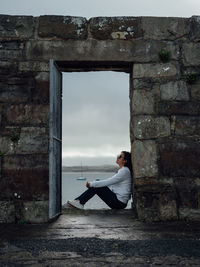 Full length of woman sitting at doorway against sky