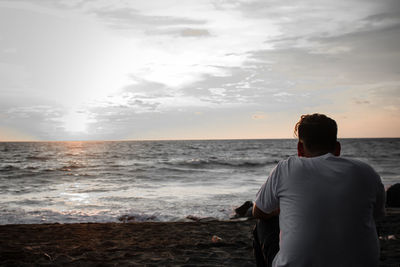 Rear view of man looking at sea against sky