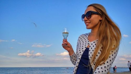 Young woman holding wineglass at sopot beach against sky