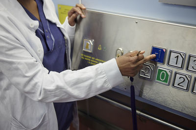 Mid section of female doctor pressing lift button