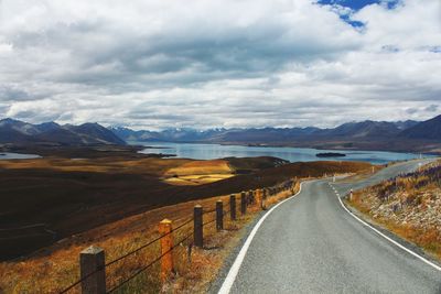 Empty road by lake against cloudy sky