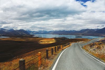 Empty road by lake against cloudy sky