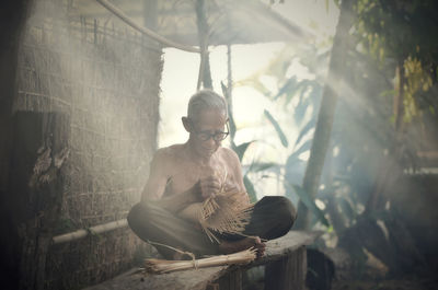 Senior man making wicker basket on sunny day