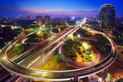 High angle view of light trails on road amidst buildings in city at night