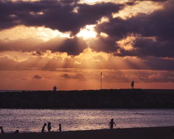 Silhouette children at beach against sky during sunset