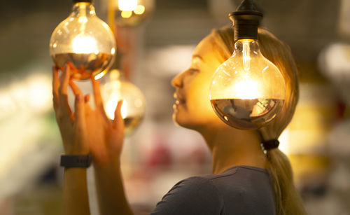 Side view of woman touching glowing light bulb