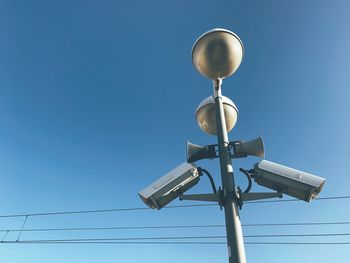 Low angle view of security camera and cables against clear blue sky