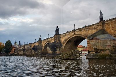 Arch bridge over river against cloudy sky