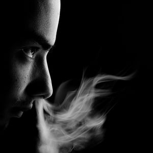 Close-up portrait of man smoking against black background