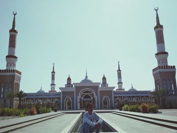 Man sitting on footpath against mosque