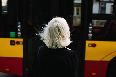 Rear view of woman standing against bus in city