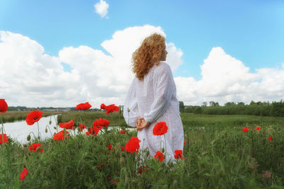 Rear view of pregnant woman standing amidst flowering plants on field against sky