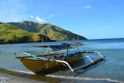 Outrigger boat moored at beach against blue sky on sunny day