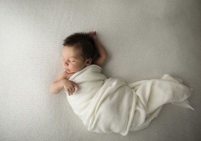 Candid newborn baby with long hair sleeps in white swaddle