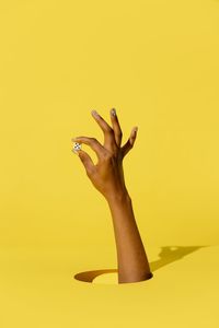 Close-up of woman hand against yellow background