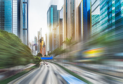 Light trails on city street by buildings against sky at dusk