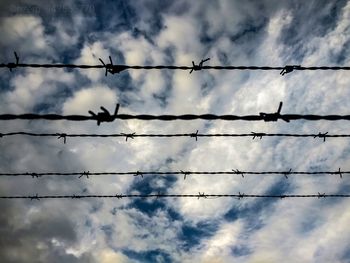 Low angle view of silhouette barbed wire against cloudy sky