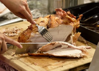 Cropped hand of woman carving turkey on cutting board